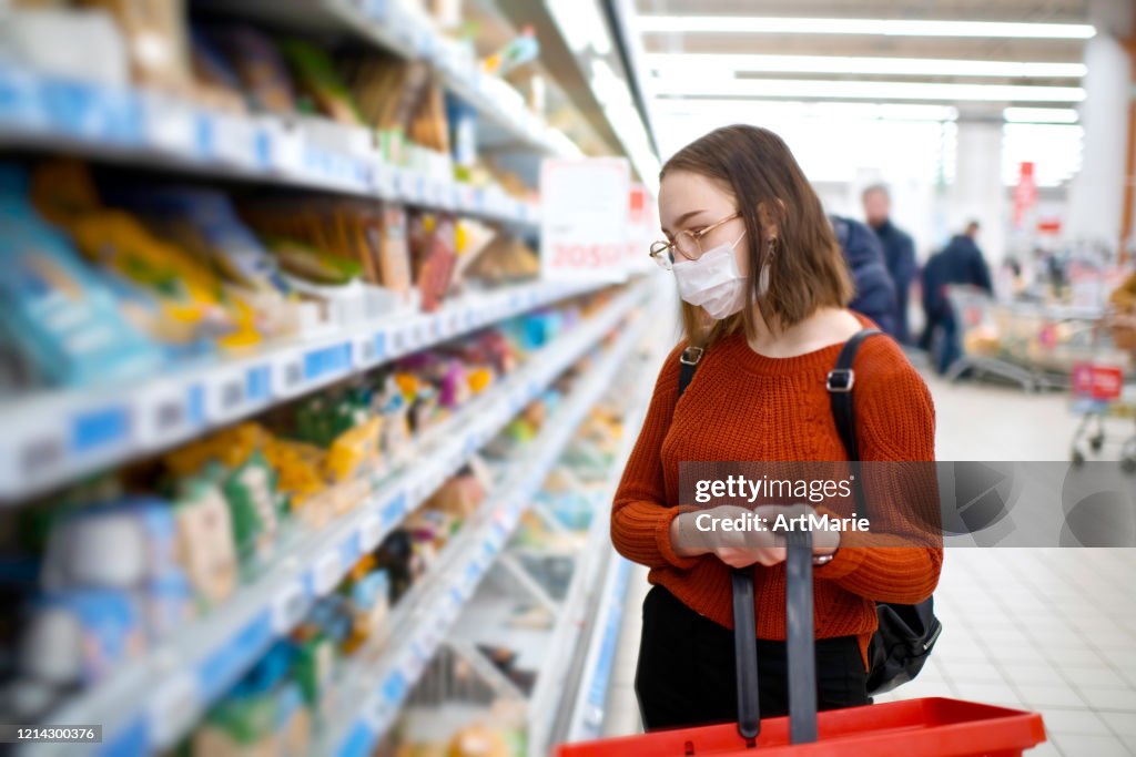 Jonge vrouw die in een kruidenierswinkelwinkel winkelwinkel winkelt en beschermend medisch masker draagt