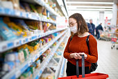 Young woman shopping in a grocery store and wearing protective medical mask