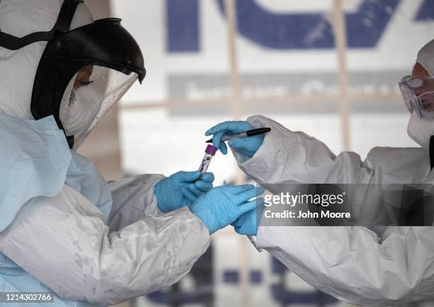 Health workers dressed in personal protective equipment handle a coronavirus test at a drive-thru testing station at Cummings Park on March 23, 2020...