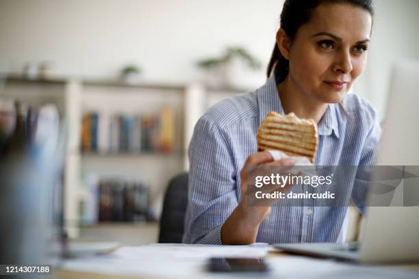 rijpe vrouw die van huis werkt - eating bread stockfoto's en -beelden