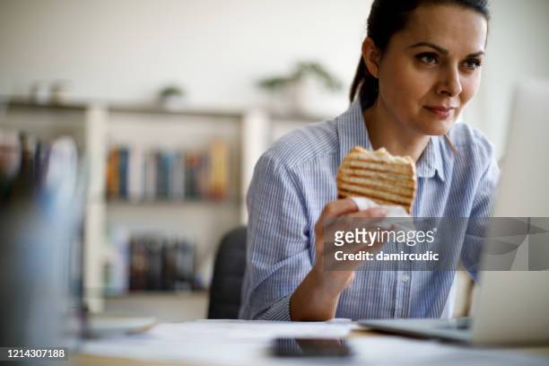 mature woman working from home - woman eating toast stock pictures, royalty-free photos & images