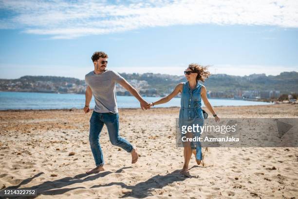 coppia che si diverte e si tiene per mano sulla spiaggia - la valletta foto e immagini stock