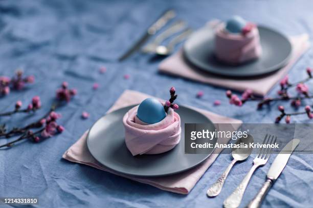 easter table setting with blue natural linen tablecloth, dinnerware, peach flowers, easter egg in pink napkins like nest. pastel colored photo taken from above. idea easter decor. - easter decoration home stock pictures, royalty-free photos & images