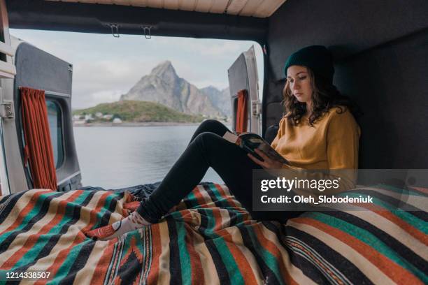 woman reading book in camper van with view on seaside on lofoten island - paperback stock pictures, royalty-free photos & images