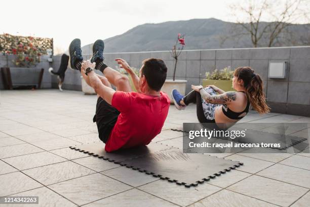 mature man and young woman doing crunches with sportswear on the terrace of his house at sunset - sit up foto e immagini stock