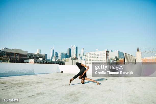 male yogi doing headstand on rooftop overlooking cityscape - flexible stock-fotos und bilder