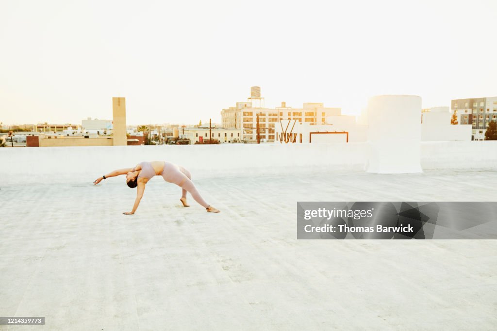Woman doing yoga on rooftop at sunset