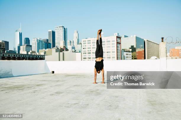 male yogi doing handstand on rooftop with city skyline in background - handstand photos et images de collection