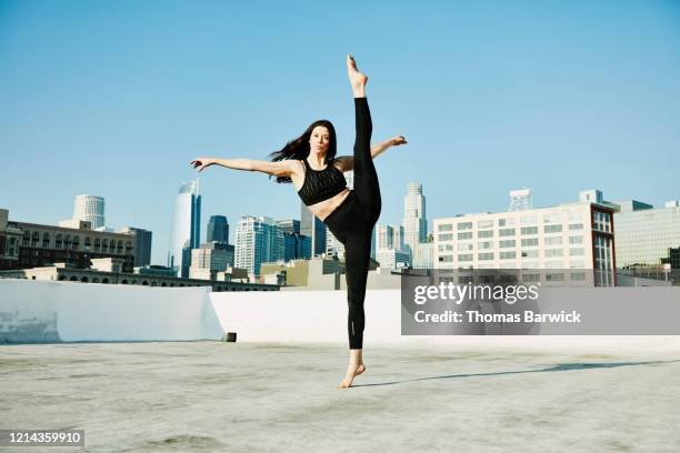 female dancer balancing on one leg while performing on rooftop overlooking city - tiptoe stock-fotos und bilder