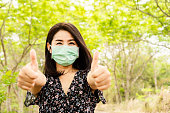 Asian woman wearing face mask walking outdoors to prevent virus covid-19  with thump up hand