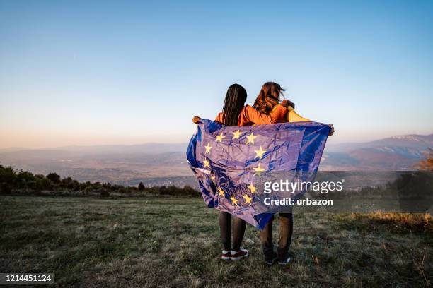 twee multi-etnische vrouwen die de vlag van de europese unie houden - harmonie stockfoto's en -beelden