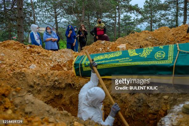 Morgue workers, wearing protective suits and face masks, dig the grave of a person who died of COVID-19, as relatives gather around on May 21 at a...