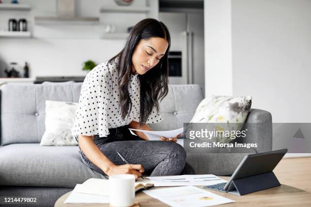 mujer analizando documentos mientras está sentada en casa - ahorro fotografías e imágenes de stock