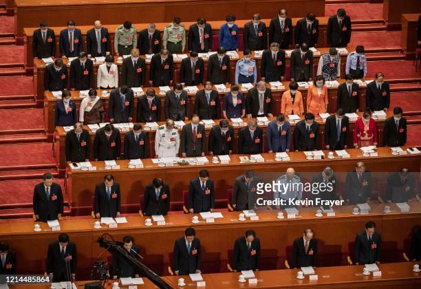 Chinese president Xi Jinping, center left, and top members of government and delegates, many wearing masks, bow their heads as they observe one...
