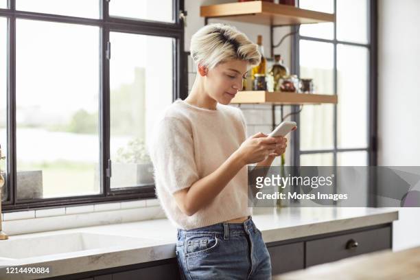 a woman using smart phone in kitchen - short hair stock pictures, royalty-free photos & images