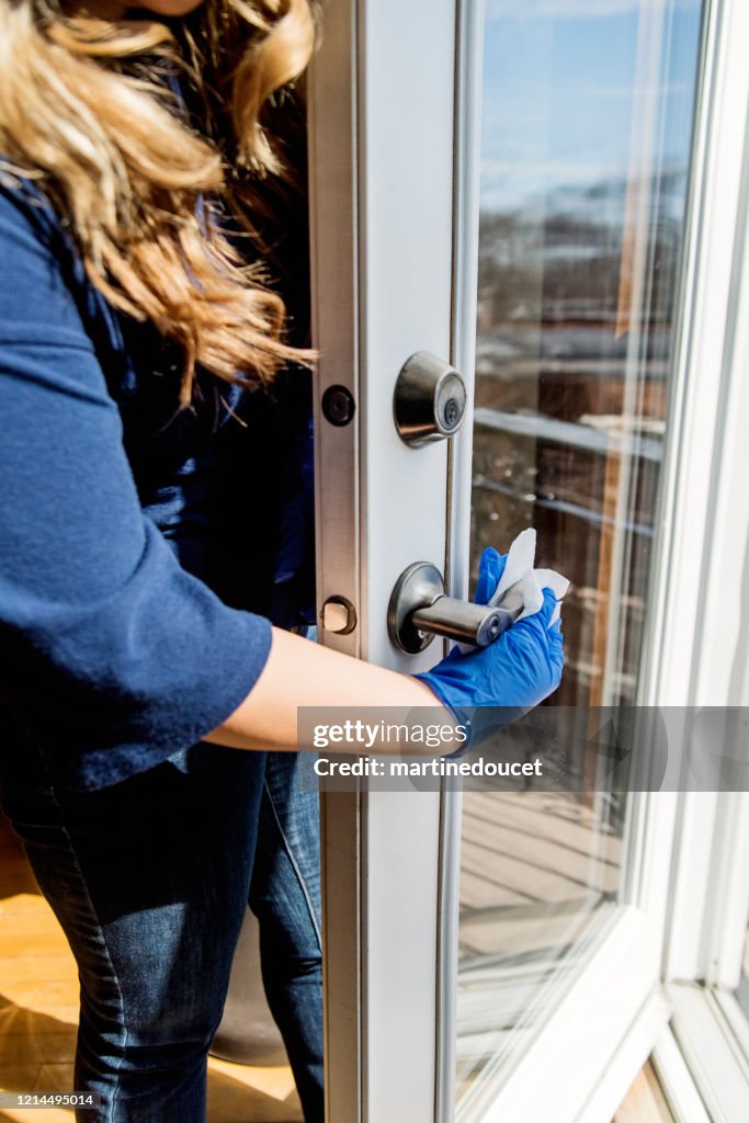 Vrouw met handschoenen die deurgreep afvegen.