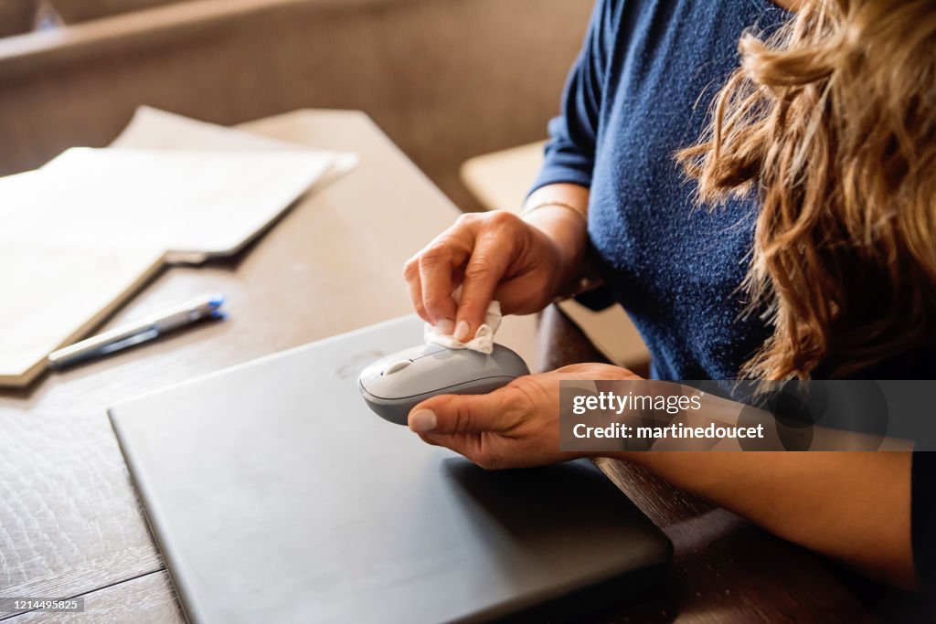 Woman hands wiping computer mouse while working from home.