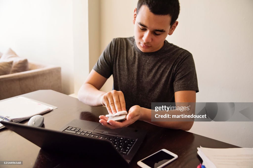 Adolescente limpiando el teléfono móvil mientras estudiaba desde casa.