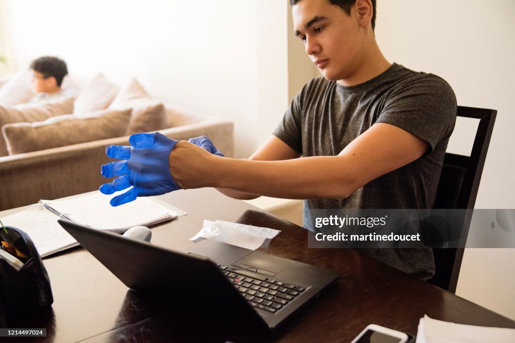 Tiener die handschoenen aantrekt om laptop af te vegen terwijl het bestuderen van huis.