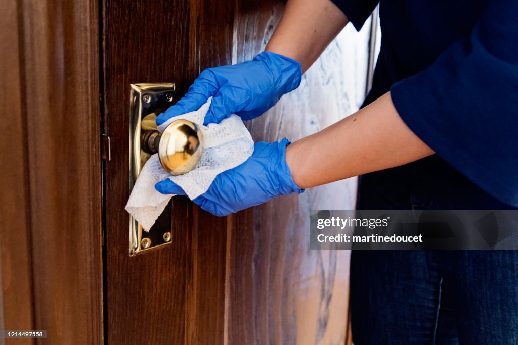 Manos con guante limpiando pomo de la puerta de madera.