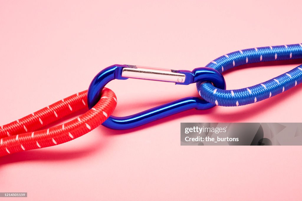 Blue carabiner with red and blue ropes on pink background