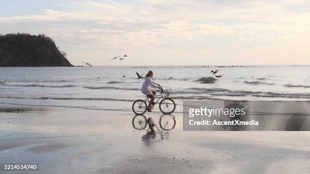 de vrouw berijdt fiets onderaan tropisch strand bij zonsopgang - groep fietsers stockfoto's en -beelden