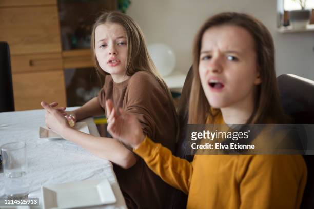teenage sisters expressing annoyance during an argument at a dining table - sibling stock pictures, royalty-free photos & images