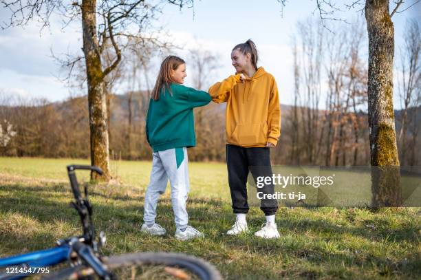 two school girls using elbow bump as an alternative handshake outdoors in nature - covid handshake stock pictures, royalty-free photos & images