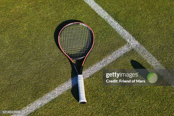 tennis racket still life with long shadow on grass lawn tennis court - tennisschläger stock-fotos und bilder