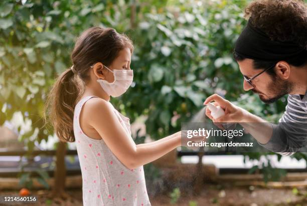 pai esguicha desinfetante para as mãos da filha, menina usa máscara facial durante coronavírus e surto de gripe - hand sanitiser - fotografias e filmes do acervo