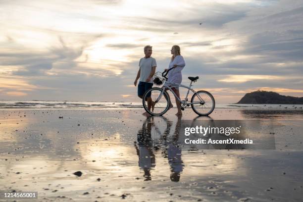 het rijpe paar duwt fiets onderaan strand bij zonsopgang - early retirement stockfoto's en -beelden