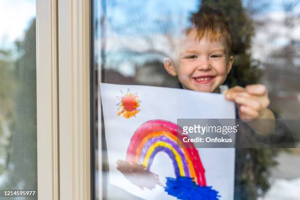 jonge jongen die zijn tekening op huisvenster tijdens de crisis covid-19 plakt - positieve emotie stockfoto's en -beelden