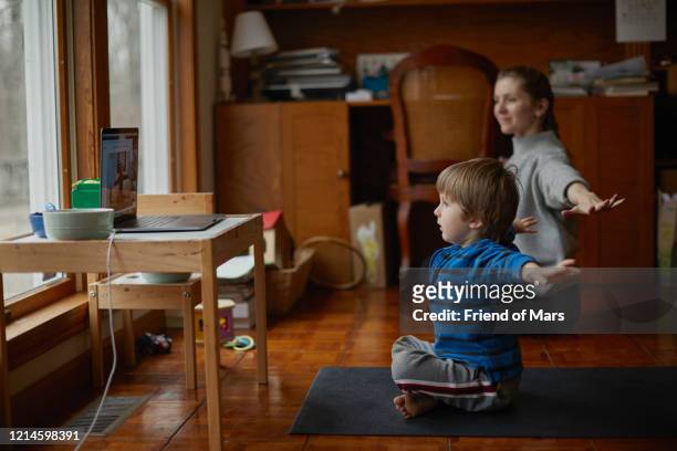Boy takes yoga class with laptop at home with mother and arms outstretched