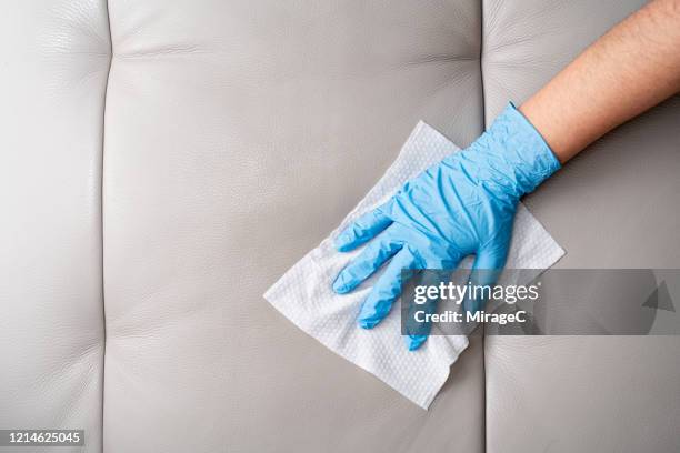 hands with glove wiping leather sofa with disinfection wipes - hand rubbing stockfoto's en -beelden