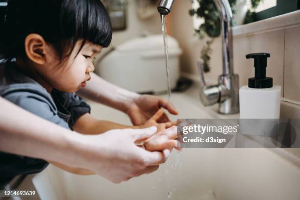 cropped shot of a mother and little daughter maintaining hands hygiene and washing their hands with soap together in the sink - washing hands photos et images de collection