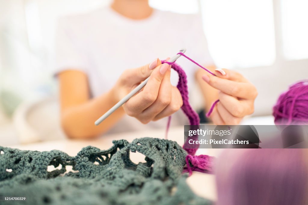 Close up young woman crocheting with needle and wool