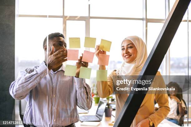 black man and muslim woman discuss their project with a help of pictures. - culture work stock pictures, royalty-free photos & images