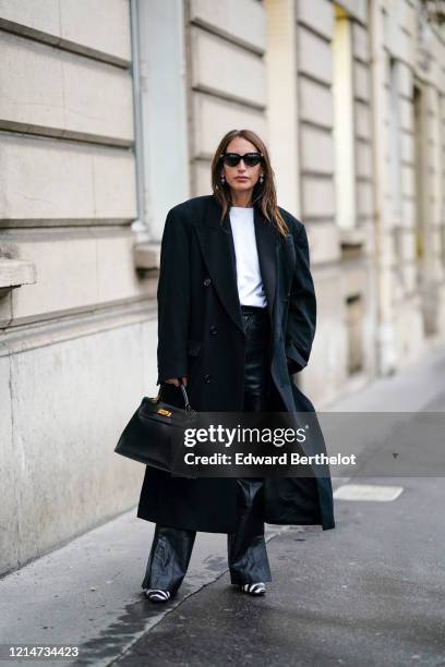 Chloe Harrouche wears sunglasses, an oversized long coat, a white t-shirt, black leather flared pants, black and white zebra print pointy shoes, a...