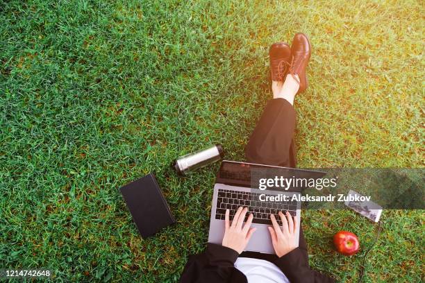 a girl in the park sitting on the grass and working on a laptop, a woman's hands on the keyboard. near mobile phone, apple, notebook. student studying outdoors. distance learning concept - college girl pics ストックフォトと画像