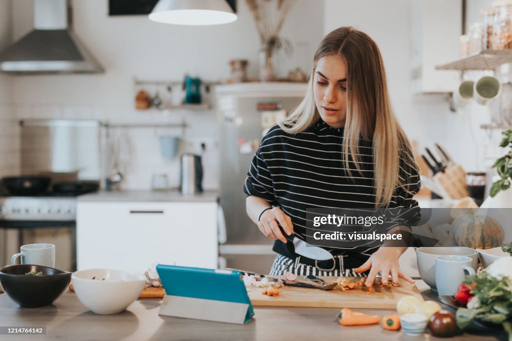Cute female teenager cooks dinner while having a video call conversation