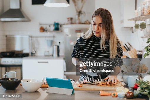 Cute female teenager cooks dinner while having a video call conversation Cute female teenager cooks dinner while having a video call conversation