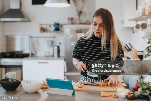 cute female teenager cooks dinner while having a video call conversation - cute 15 year old girls stock pictures, royalty-free photos & images