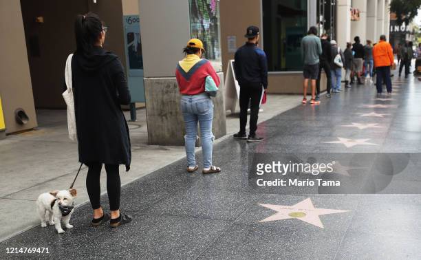People maintain social distancing while standing in line to enter a Trader Joe's, along the Hollywood Walk of Fame, as the coronavirus pandemic...
