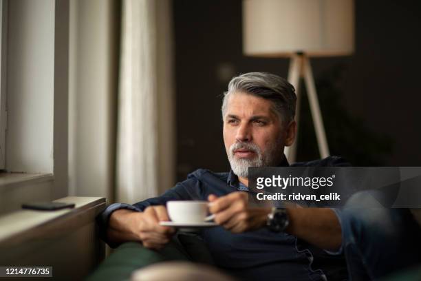 a man by the window holding a cup of coffee. - coffee moustache stock pictures, royalty-free photos & images