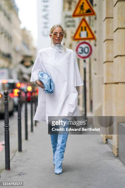 Leonie Hanne wears white sunglasses with chains, a white long dress, a pale blue puff Bottega Veneta bag, blue suede thigh high pointy boots, outside...