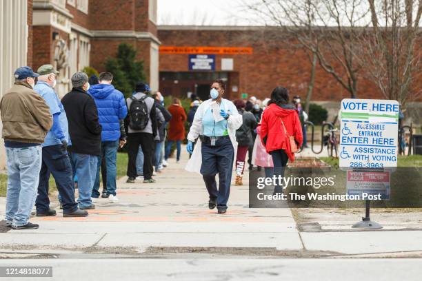 Woman hands out surgical masks to people standing in line to vote in Wisconsins spring primary election on Tuesday, April 7, 2020 at Riverside High...