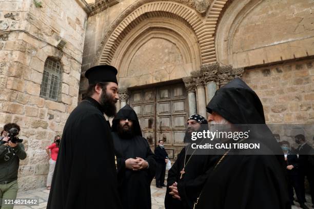 Greek Orthodox, Armenian, and Coptic Orthodox Christian clergymen speak together while standing outside the Church of the Holy Sepulchre in...