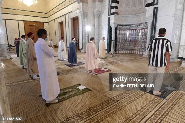 Tunisian imam leads in prayer with other worshippers seated in predetermined spaces inside a mosque, in adherence to social distancing rules due to...