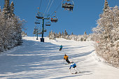 view of skiers on ski lift with snow covered mountains chairlift above ski slope