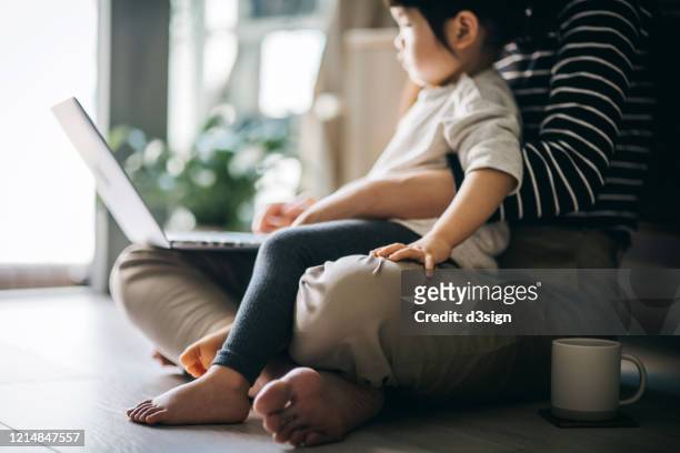 cropped shot of a young asian mother using laptop and working from home while taking care of little daughter in self isolation during the covid-19 health crisis - woman home with sick children imagens e fotografias de stock